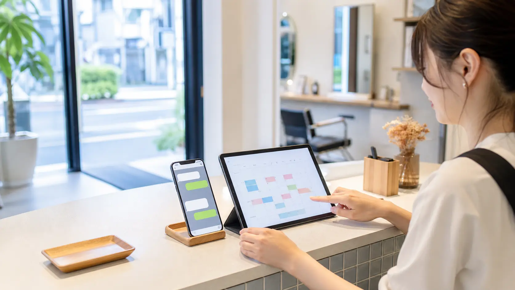 店舗受付でスマートフォンのチャット自動返信とタブレットの予約管理を確認している様子